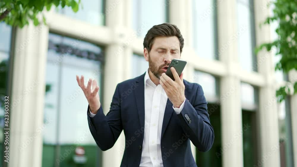 Angry businessman talking emotionally while holding smartphone while standing outside. Shirty irate mature male boss entrepreneur in formal suit is arguing on the phone in front of an office building Angry businessman talking emotionally while holding smartphone while standing outside. Shirty irate mature male boss entrepreneur in formal suit is arguing on the phone in front of an office building