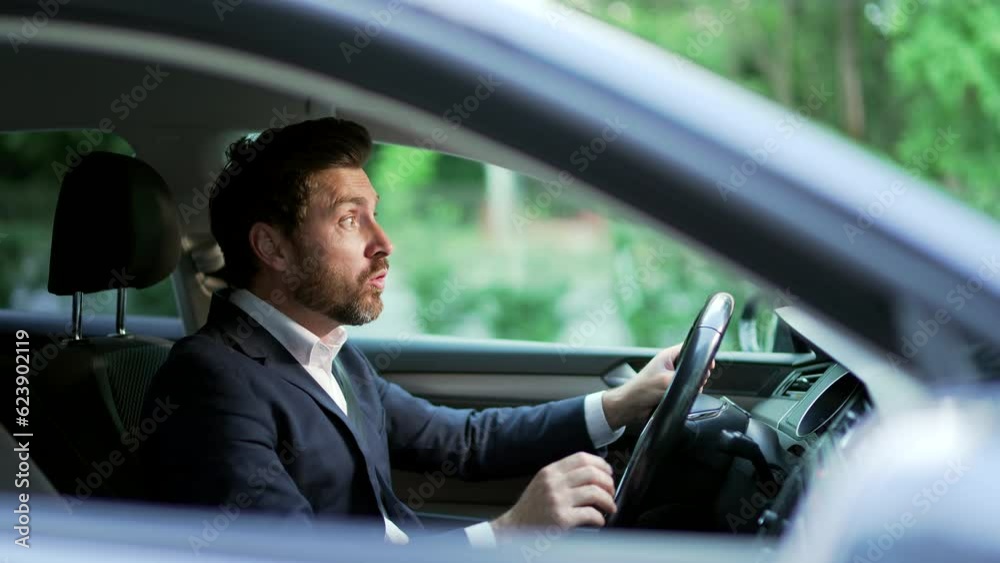 Furious angry man standing in a traffic jam beeps and hurries. Sitting in the car. Irritated nervous mature adult business male in suit tired driver in automobile. Stressful commuting to be late work Furious angry man standing in a traffic jam beeps and hurries. Sitting in the car. Irritated nervous mature adult business male in suit tired driver in automobile. Stressful commuting to be late work