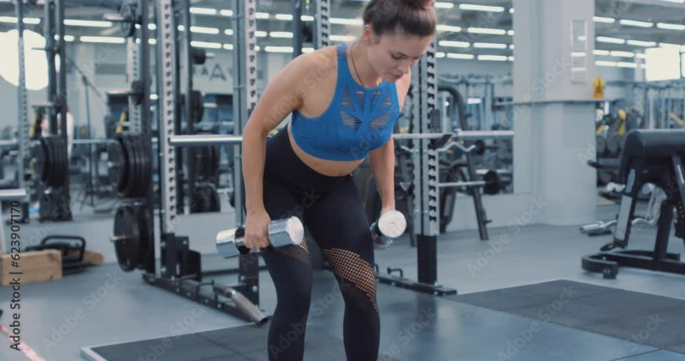 Fit serious motivated woman in sportswear bending forward and lifting dumbbells, equipment on background. female athlete working out in gym. back workout Slow motion Side view Fit serious motivated woman in sportswear bending forward and lifting dumbbells, equipment on background. female athlete working out in gym. back workout Slow motion Side view