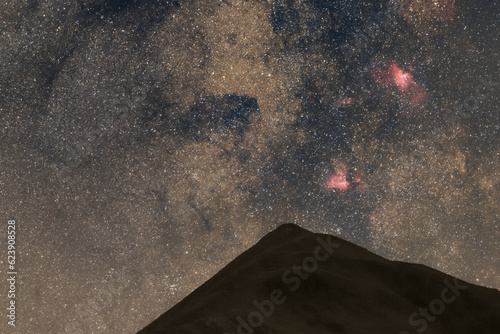 Stars at the night sky with M16 and M17 nebulae in the constellation of Sagittarius over a mountain peak of the Pyrenees, France photo