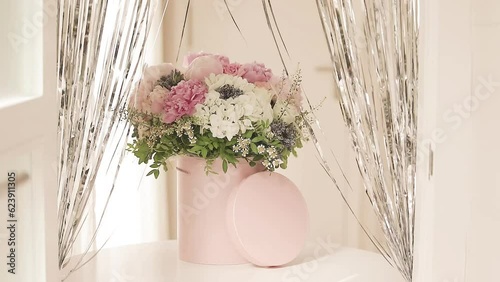 An elegant bouquet of fresh roses, peonies, and daisies in a pink box, beautifully arranged and placed by a light-filled window.