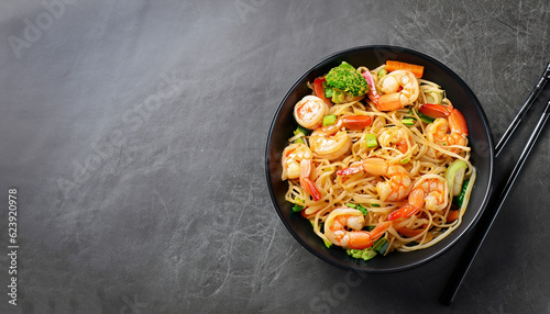 Stir fry noodles with vegetables and shrimps in black bowl. Slate background. Top view. Copy space.