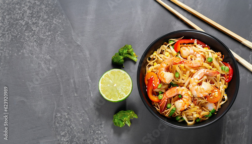 Stir fry noodles with vegetables and shrimps in black bowl. Slate background. Top view. Copy space. photo