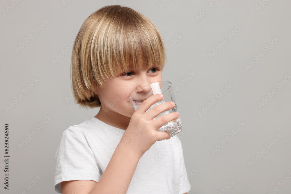 Cute little boy drinking fresh water from glass on light grey background, space for text Cute little boy drinking fresh water from glass on light grey background, space for text