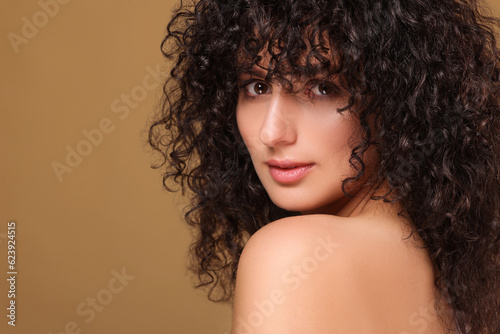 Beautiful young woman with long curly hair on beige background. Space for text