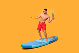 Man with pineapple posing on SUP board against orange background