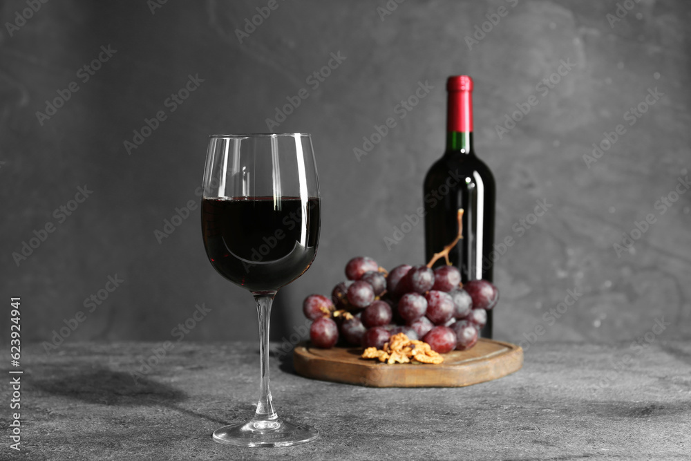 Obraz premium Glass of red wine, bottle, nuts and grapes on grey table