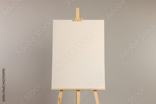 Wooden easel with blank canvas on grey background
