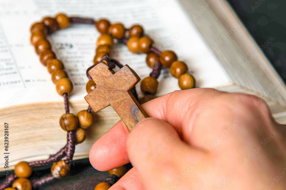 Fototapeta premium Hand holding and praying on rosary, on Bible background