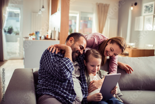 Young family using a digital tablet at home together while sitting on the couch in the living room
