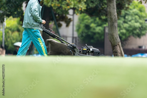 Worker is mowing the lawn with a lawn mower