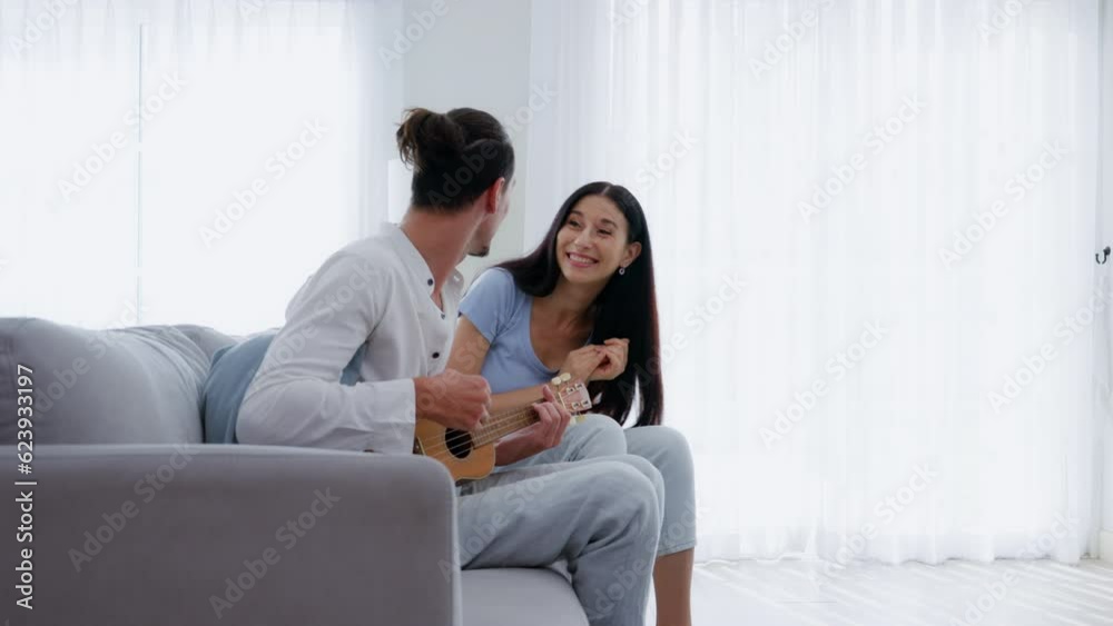 Happy couple lover singing a song playing guitar on sofa in living room at home Happy couple lover singing a song playing guitar on sofa in living room at home