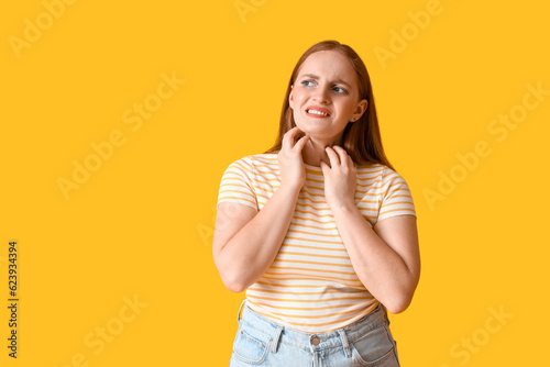 Allergic young woman scratching on yellow background