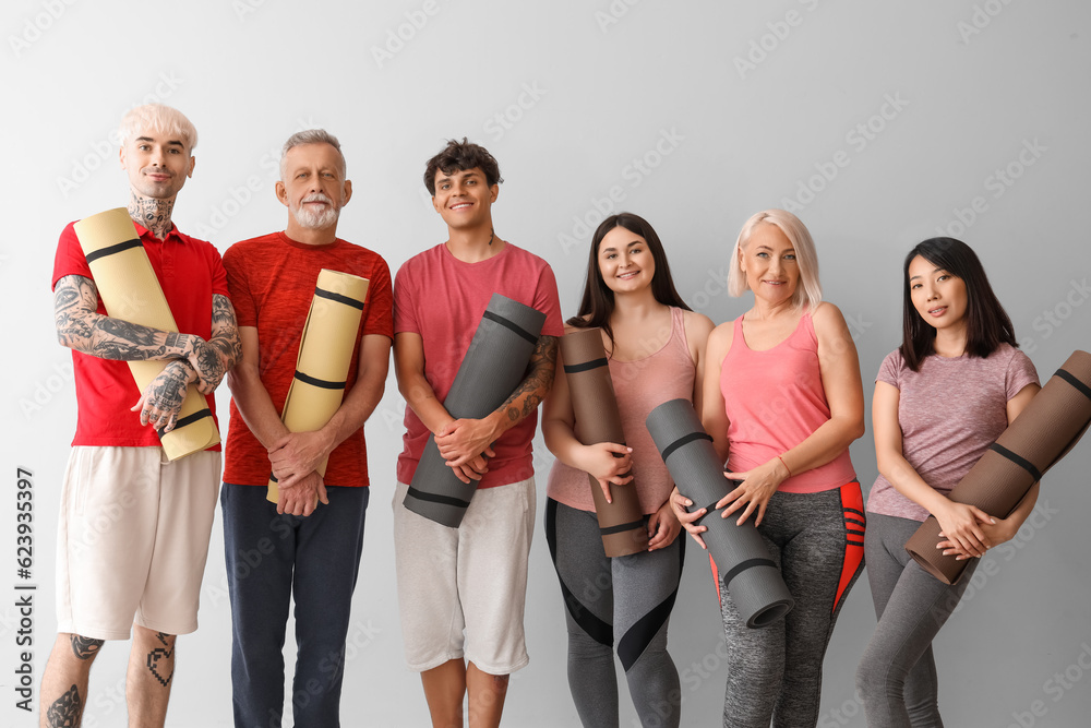 Obraz premium Group of sporty people with fitness mats on light background