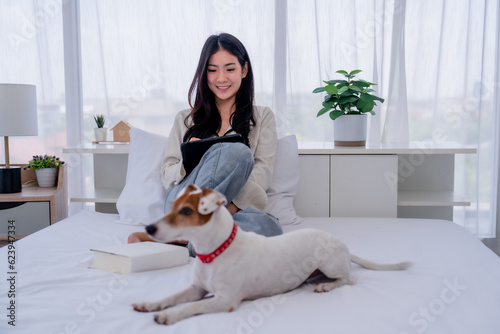 Asian Woman Working from the Comfort of Her Bedroom with Her Adorable Pet by Her Side © Jirakul