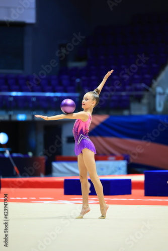 girl gymnast performs an exercise with a ball