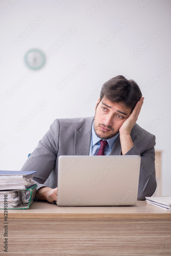 Young male employee unhappy with excessive work in the office Young male employee unhappy with excessive work in the office