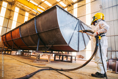 Steel Grit blasting process, Industial worker using steel grit blasting process preparation cleaning surface on steel structure before painting in factory workshop.