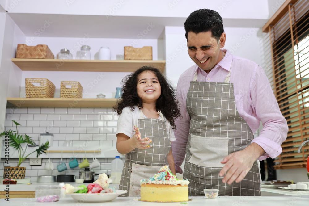 Happy lovely asian single dad and cute daughter in apron having fun with teaching and decorating homemade cake in the kitchen. Family lifestyle cooking with education concept.