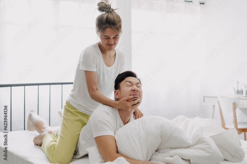Fototapeta premium Funny asian couple wife giving husband hurt massage in white bedroom.