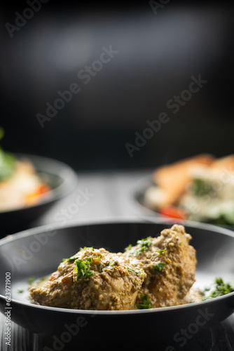 Chicken breast in creamy garlic sauce in plate on lack background with other dishes