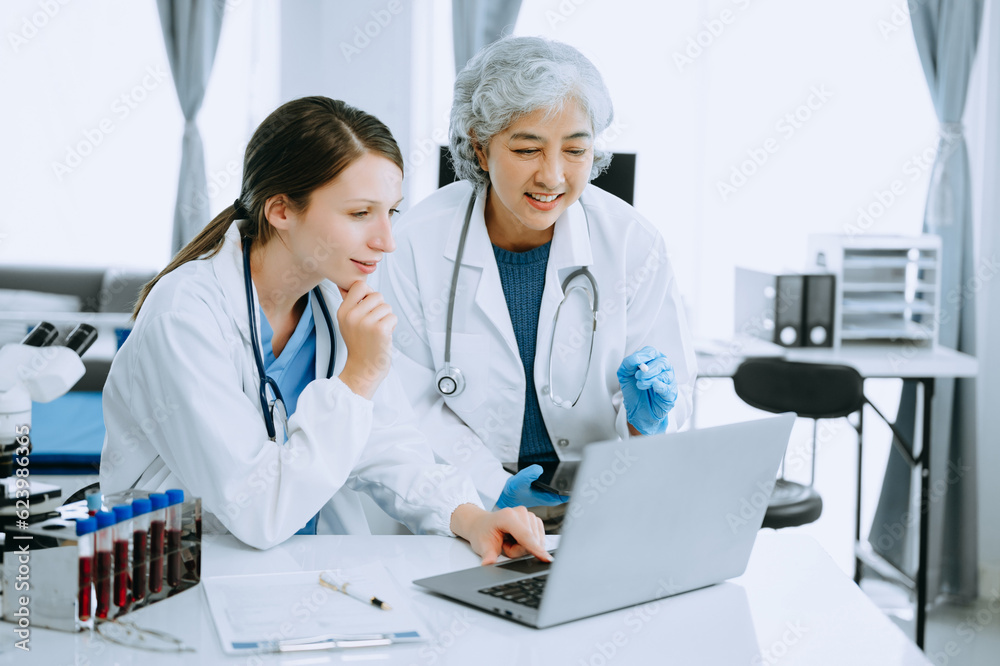 Medical team having a meeting with doctors in white lab coats and surgical scrubs seated at a table discussing a patients working online using computers in the medical industry.. Medical team having a meeting with doctors in white lab coats and surgical scrubs seated at a table discussing a patients working online using computers in the medical industry..