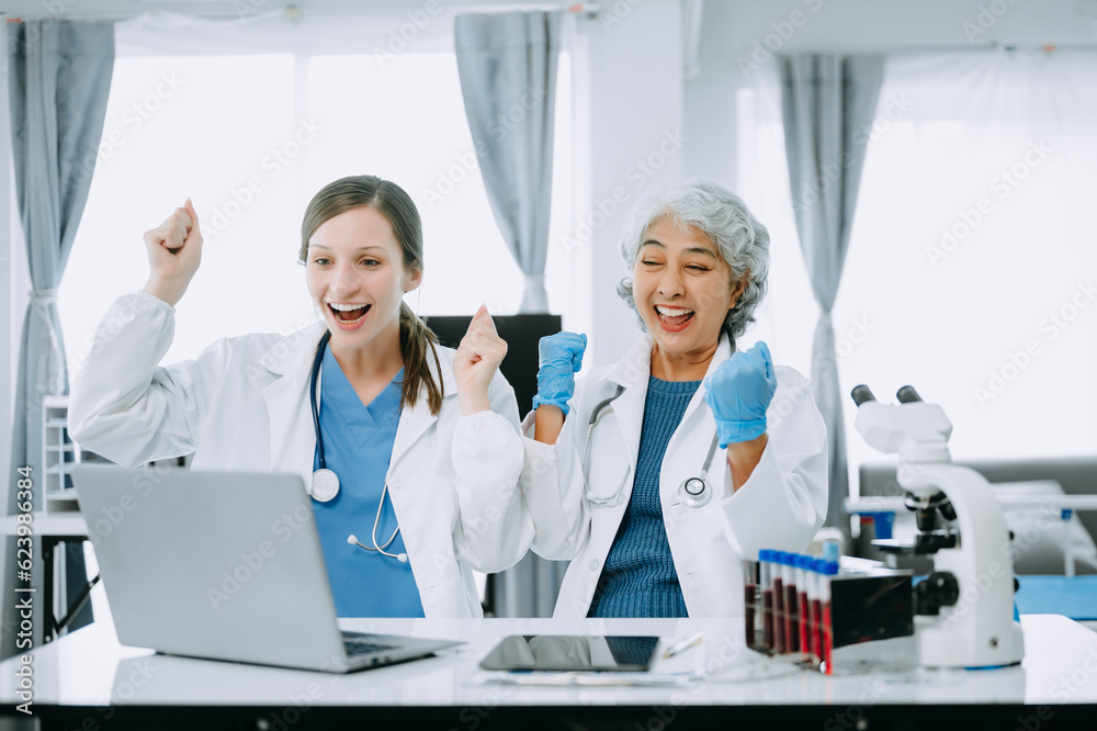 Medical team having a meeting with doctors in white lab coats and surgical scrubs seated at a table discussing a patients working online using computers in the medical industry.. Medical team having a meeting with doctors in white lab coats and surgical scrubs seated at a table discussing a patients working online using computers in the medical industry..