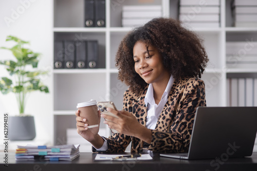 Young African American businesswoman working with smartphone  and laptop at desk in office, business finance technology concept. © SOMKID