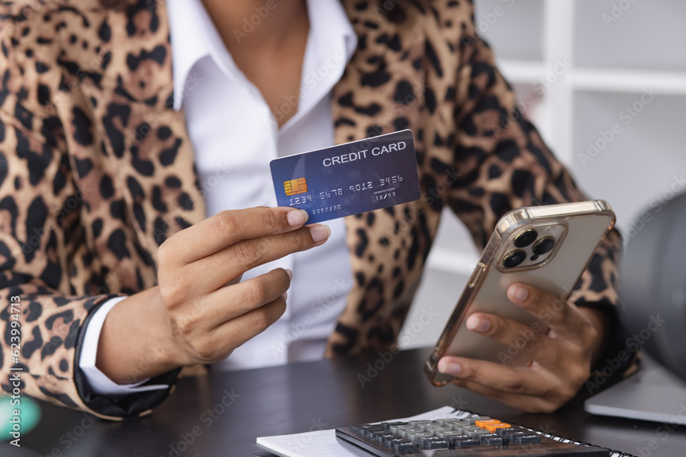 Young African American businesswoman holding credit cards with smartphone sitting at a desk in office. shopping online,