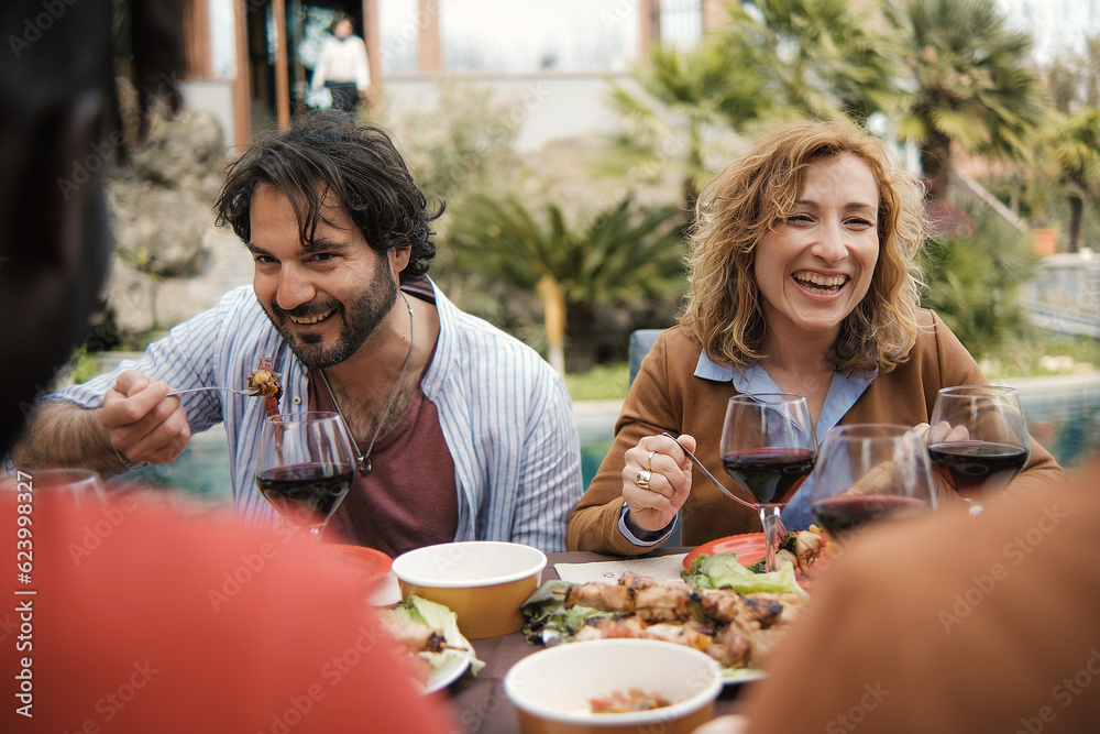 Friends Enjoying Countryside Meal - Bearded man and curly-haired woman, both in their 40s, eating, chatting at picnic table Friends Enjoying Countryside Meal - Bearded man and curly-haired woman, both in their 40s, eating, chatting at picnic table