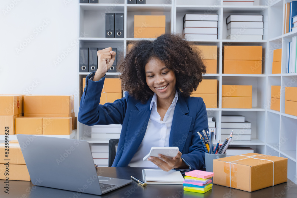 African American owner checking orders from customers sitting at desk in office, sell products online concept. African American owner checking orders from customers sitting at desk in office, sell products online concept.