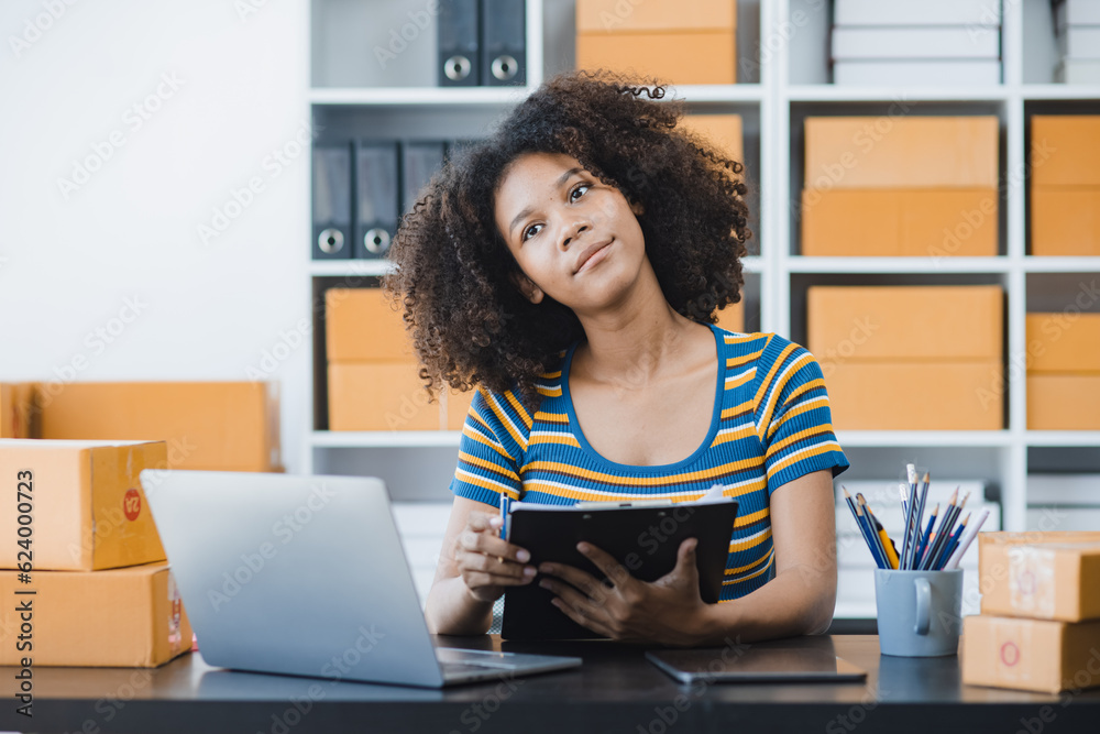 African American owner checking orders from customers sitting at desk in office, sell products online concept.