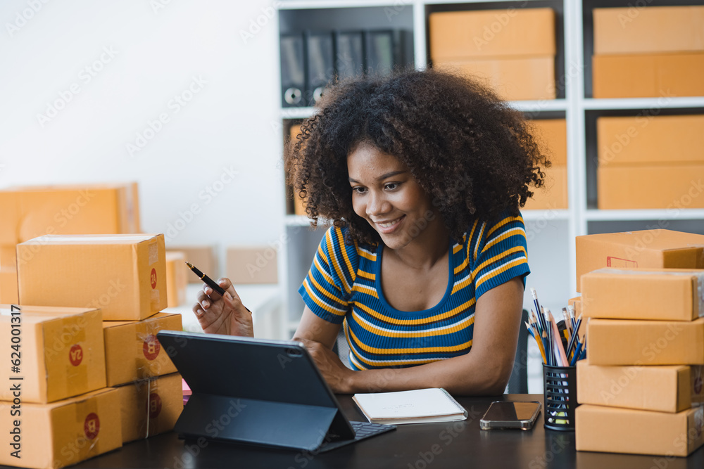 African American owner checking orders from customers sitting at desk in office, sell products online concept. African American owner checking orders from customers sitting at desk in office, sell products online concept.