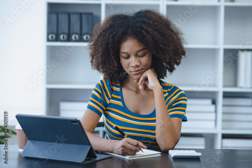 African American businesswoman holding digital tablet sitting at office desk.