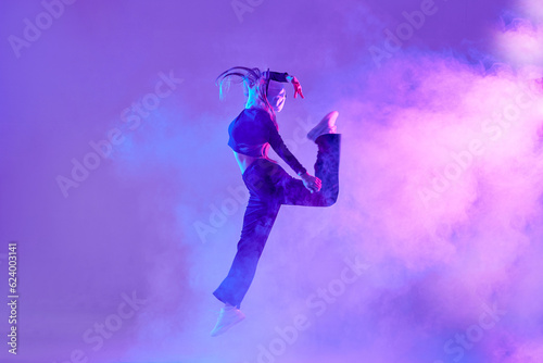 a girl in dark clothes dances on a neon background in smoke, modern dance © st.kolesnikov