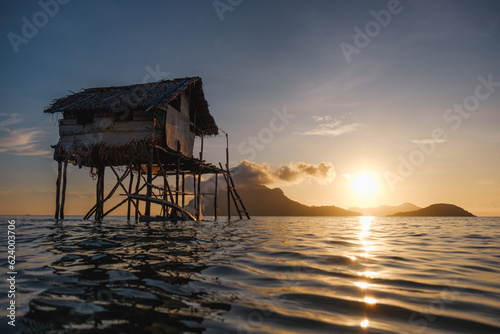 A picturesque Bajau stilt house gracefully perched above the glistening water enhanced by the breathtaking backdrop of a radiant sunrise or sunset. photo