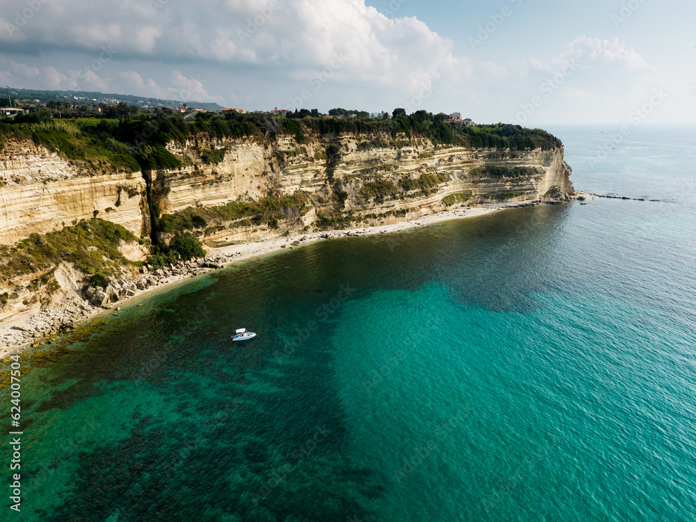 aerial view from the drone of a cliff overlooking an emerald crystalline Caribbean sea. There is also a small boat that carries bathers on vacation