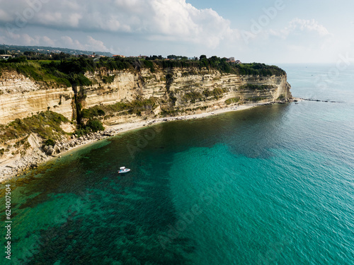 aerial view from the drone of a cliff overlooking an emerald crystalline Caribbean sea. There is also a small boat that carries bathers on vacation