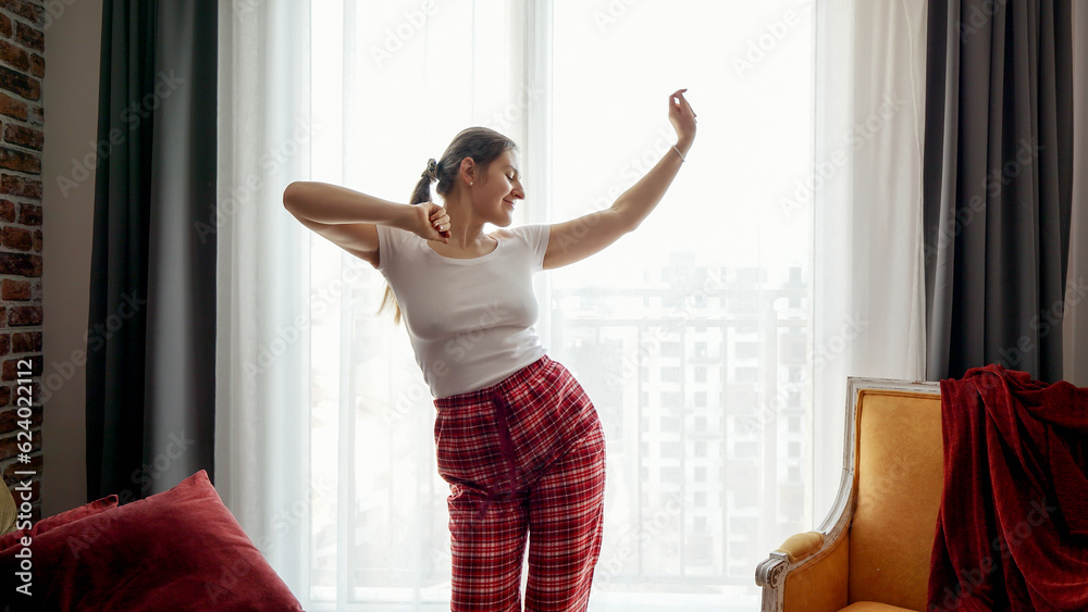 Happy smiling woman listening music and dancing in pajamas at