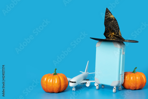 Halloween travel and tourism, trip insurance, online tours, international flights, plane and luggage in a halloween hat with pumpkins on a blue background with copy space,holidays and vacations