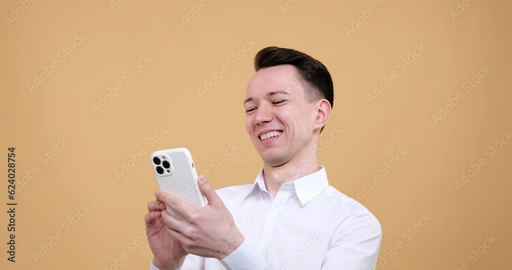 Caucasian man standing against a warm beige background. His expression transforms from astonishment to pure joy as he engages with his phone. His eyes light up laughter escapes his lips. Caucasian man standing against a warm beige background. His expression transforms from astonishment to pure joy as he engages with his phone. His eyes light up laughter escapes his lips.