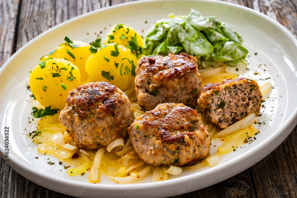 Seared pork meatballs with fried onion, boiled potatoes and lettuce in cream sauce on wooden table
Seared pork meatballs with fried onion, boiled potatoes and lettuce in cream sauce on wooden table