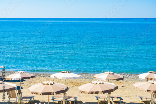 Fototapeta Naklejka Na Ścianę i Meble -  The beach of the village of Varazze, Liguria, Italy, with no people. Beach umbrellas in the foreground. Turquoise waters with blue sky on the background.