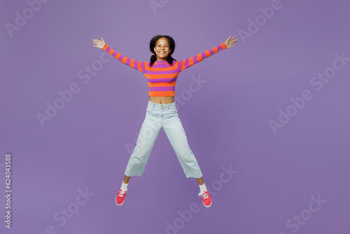 Full body cool excited happy little kid teen girl 15-16 year old wear striped orange sweatshirt jump high with outstretched hands legs isolated on plain purple background. Childhood lifestyle concept.