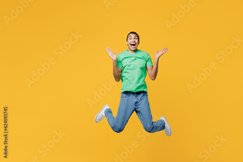 Full body young man of African American ethnicity he wears casual clothes green t-shirt hat jump high look camera spread hands isolated on plain yellow background studio portrait. Lifestyle concept. © ViDi Studio