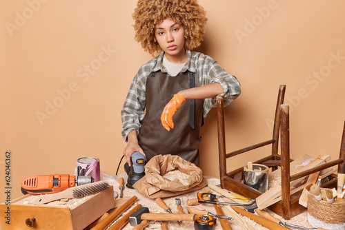 Talented serious female carpenter demonstrates her exceptional craftsmanship meticulously grinds piece of wood illustrating precision and expertise she brings to her craft transforming raw materials