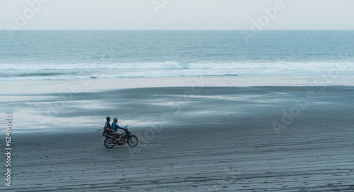 Landscape view of two unreconized bikers driving on beach with sea background. Riding a scooter on the ocean sand