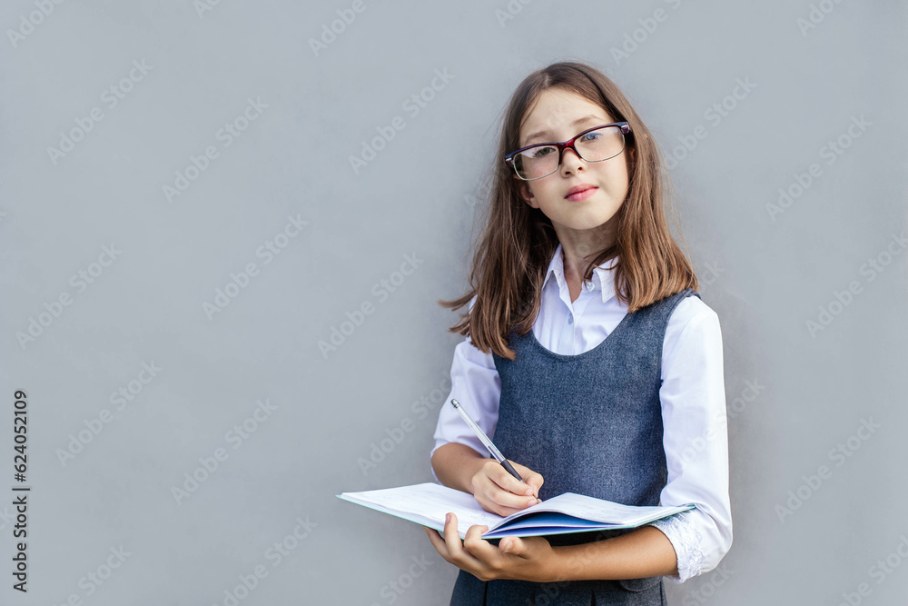 Close-up portrait of a schoolgirl holding a notebook in her hands and writing in it with a pen, looking at camera, copy space Close-up portrait of a schoolgirl holding a notebook in her hands and writing in it with a pen, looking at camera, copy space