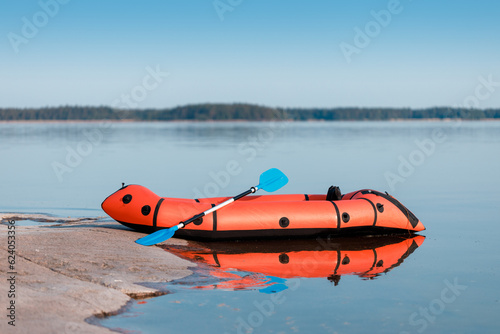 Red packraft with a paddle on the seashore.