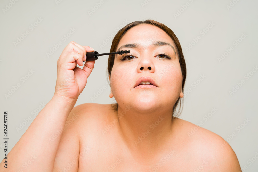 Fototapeta premium Hispanic big woman on a beauty concept putting on mascara
